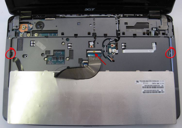Keyboard retainers circled. Arrow points to connector of keyboard to laptop. The brown clip lifts at the bottom to release the keyboard